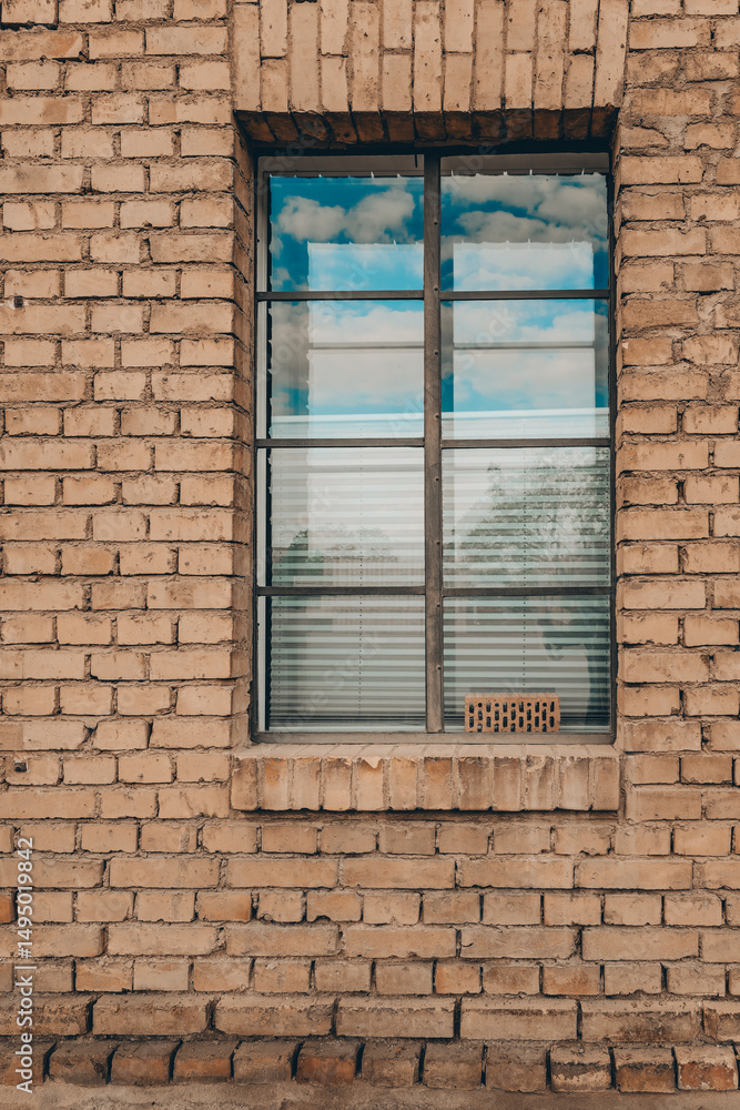 Obraz premium Reflections of clouds shimmer through a window framed by warm, textured brick in a peaceful rural setting during the afternoon