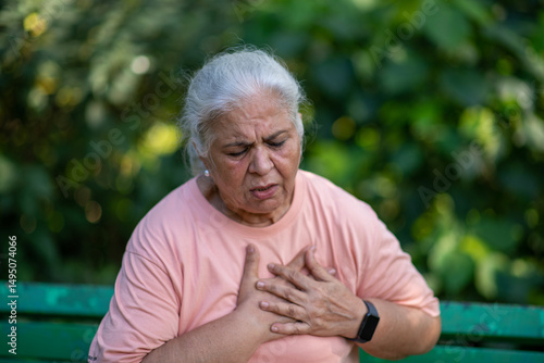 Cuadro en lienzo Indian Senior woman holding chest with pained expression sitting on bench outdoors