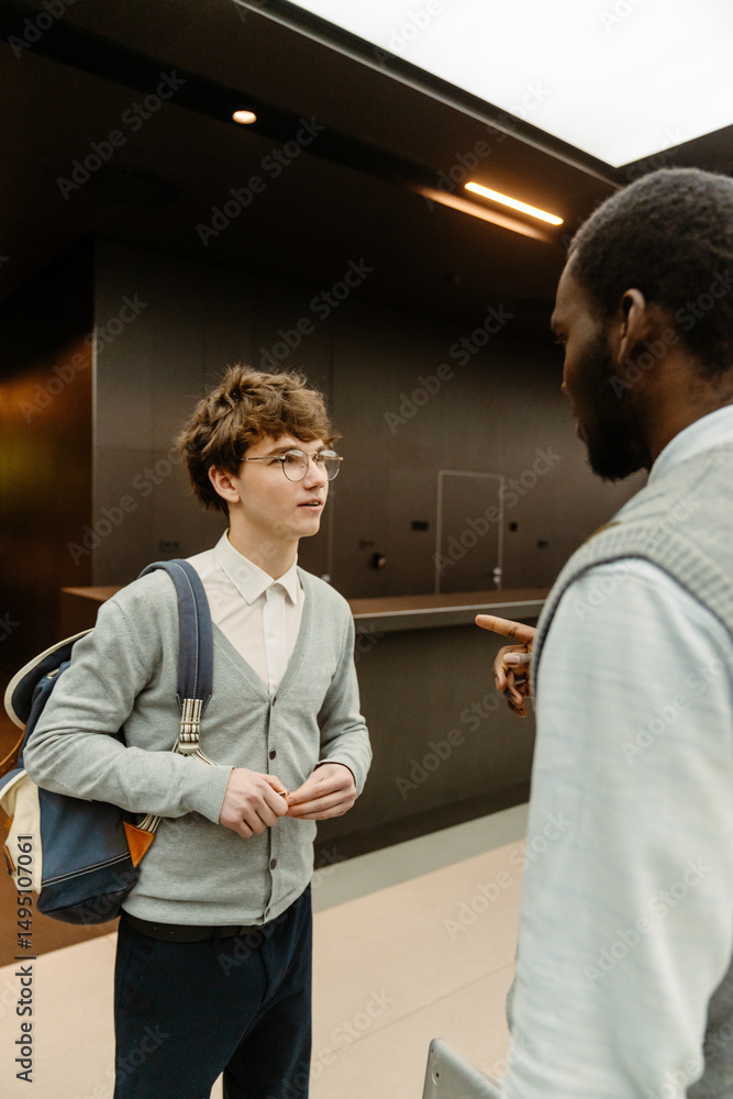 Obraz premium A male intern stands and listens to a male employee standing across from him and talking, in a hall