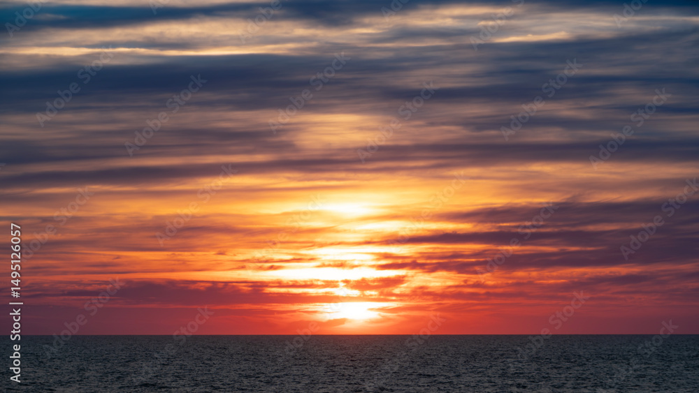 Fototapeta premium Fiery sunset over the ocean. Intense red and orange hues illuminate the sky and water, creating a stunning visual display