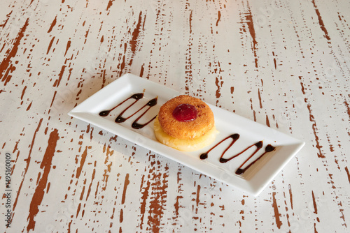 A dessert with a cherry on top is on a white plate. The plate is on a table