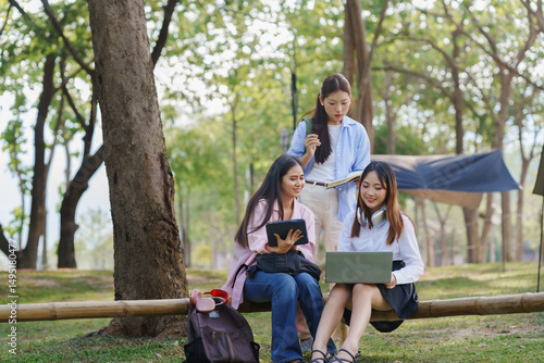Three young female students using laptop and tablet, collaborating on a project outdoors in a park