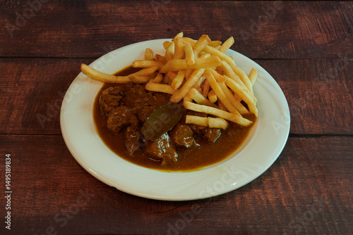 A plate of food with a piece of meat and french fries. The meat is covered in gravy and the fries are golden brown