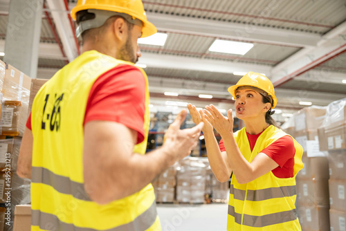 Tablou pe pânză Two warehouse workers in a dispute, showcasing emotions and communication in a hectic warehouse environment