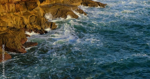 Sunlight drenches the rugged cliffs of Cascais as turquoise waves churn and foam below. The Atlantic pulses with motion, wrapping around the textured rock formations in a mesmerizing coastal dance.