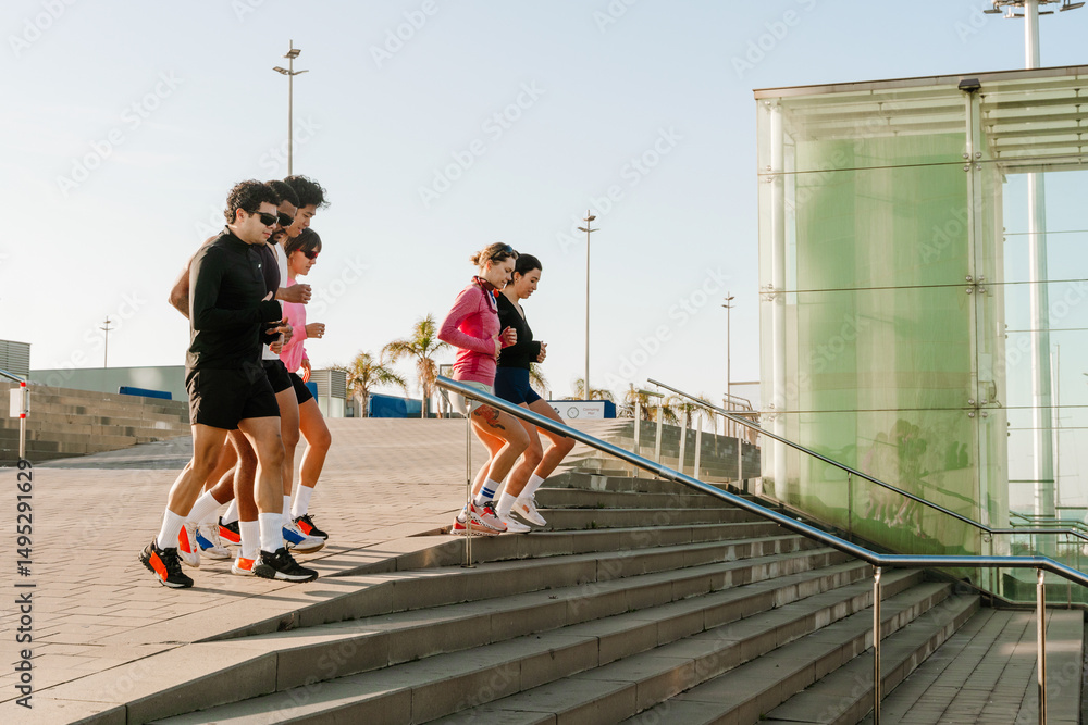 Fototapeta premium A group of six athletes run down the stairs and look ahead, on the street