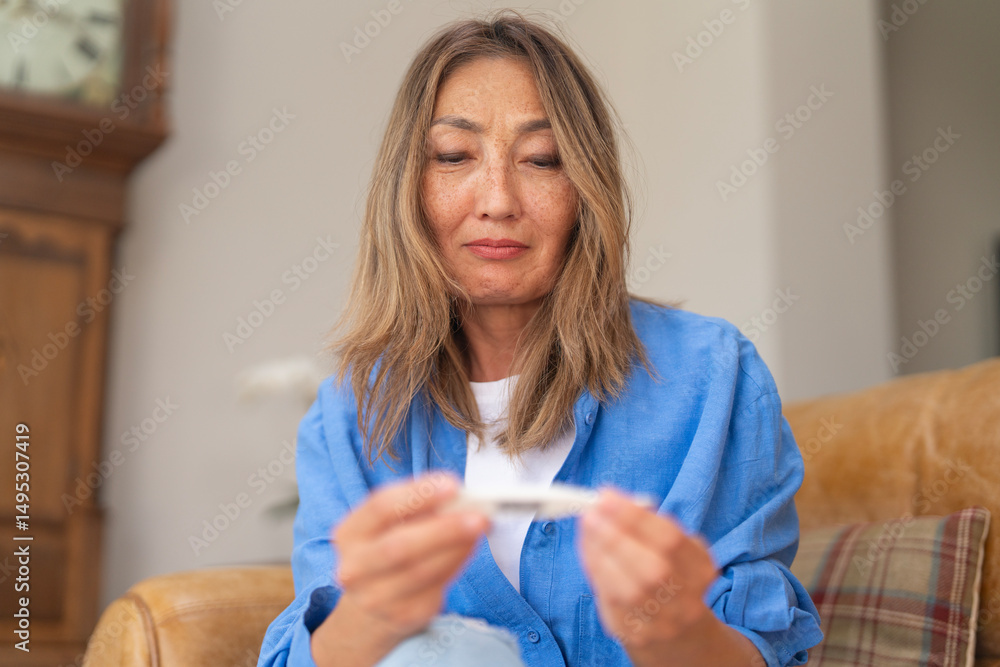 Woman checks test result at home while sitting on couch in well-lit living room during the day Woman checks test result at home while sitting on couch in well-lit living room during the day