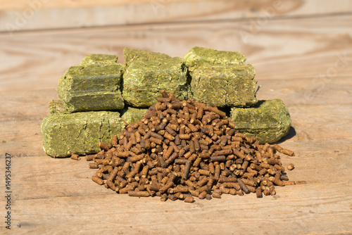 Senior horse feed; dark brown pelleted food with molasses in front, and green alfalfa cubes on the back; on wooden surface