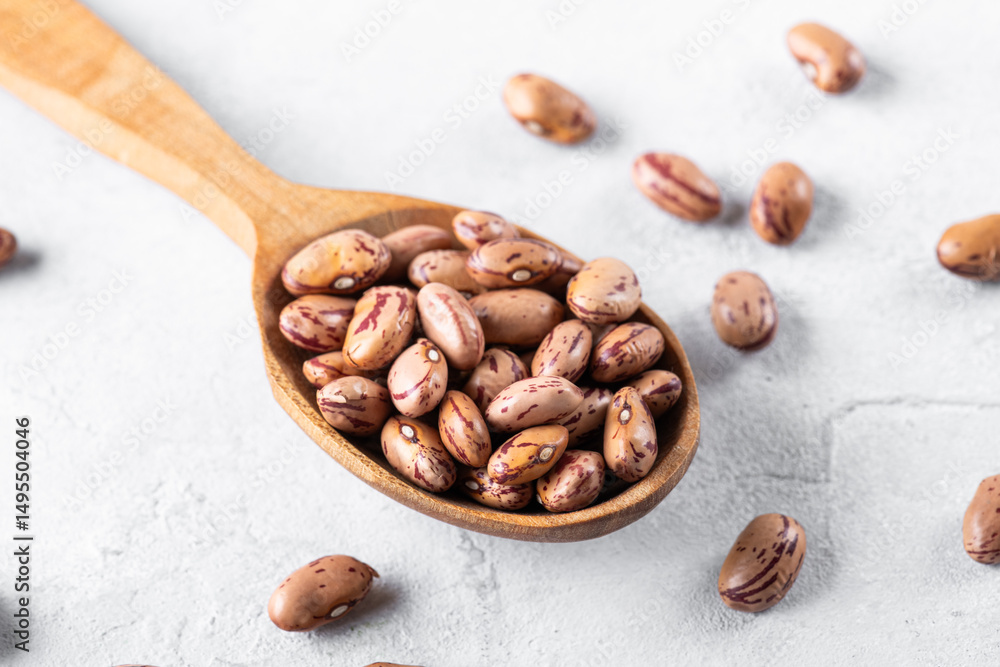 Fototapeta premium Borlotti beans on a wooden spoon on a gray table surface. Popular in Mediterranean diets, these legumes are rich in fiber and protein, often used in soups and stews