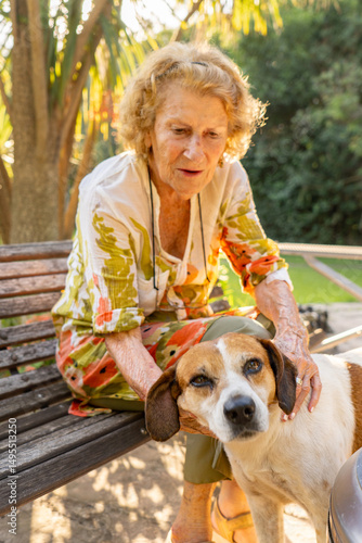 Senior woman sitting on bench petting her dog in a park