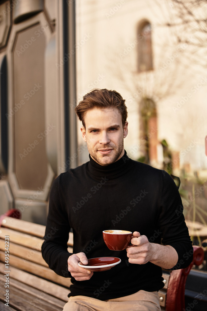Handsome man enjoying a warm drink while sitting on a bench in a vibrant urban setting Handsome man enjoying a warm drink while sitting on a bench in a vibrant urban setting