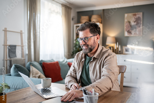 Quadro su tela Smiling mature professional working remotely from home office using laptop