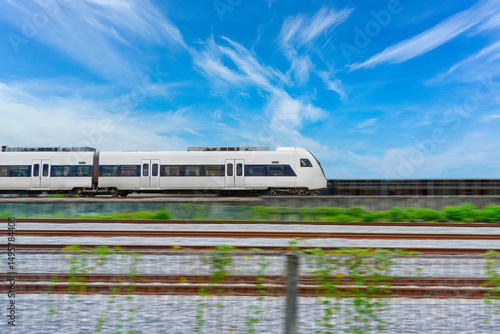 Speed modern commuter train, motion blur rides among the fields and green vegetation. with blue sky clouds, side view.