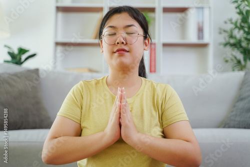 Asian woman meditate and practice yoga in the living room at home, home health care, exercise.