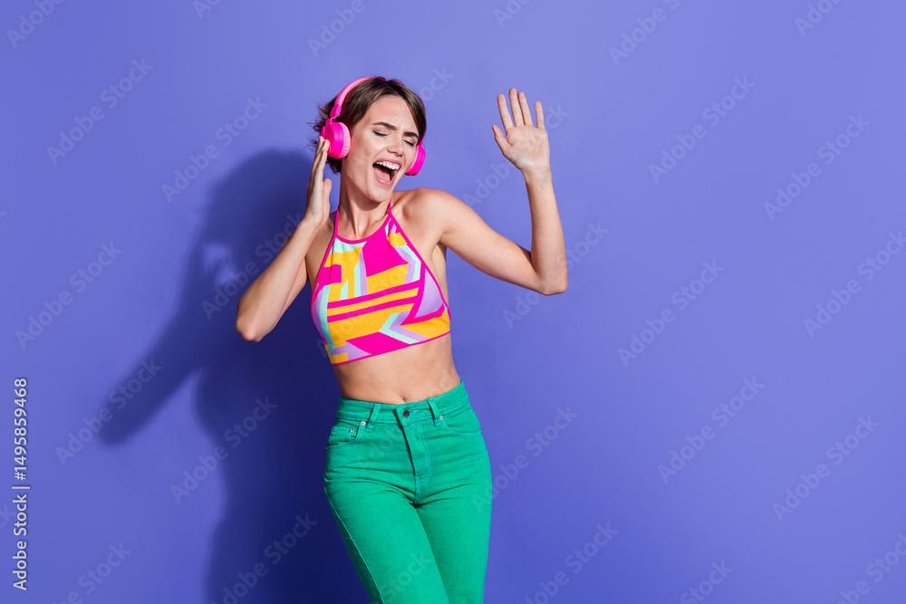 Fototapeta premium Photo of young energetic girl in pink crop top stylish outfit dancer likes wireless headphones isolated on violet color background