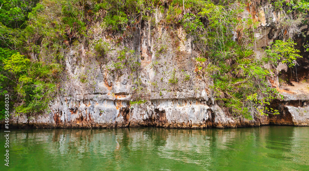 Fototapeta premium Samana bay view. A rocky cliff positioned by a tranquil green water
