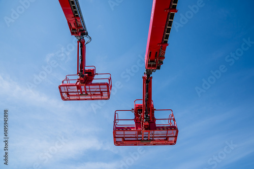 Two red large industrial telescopic construction lift platforms side by side on blue skies in the background, construction industry developing with modern machinery for lifting high up
