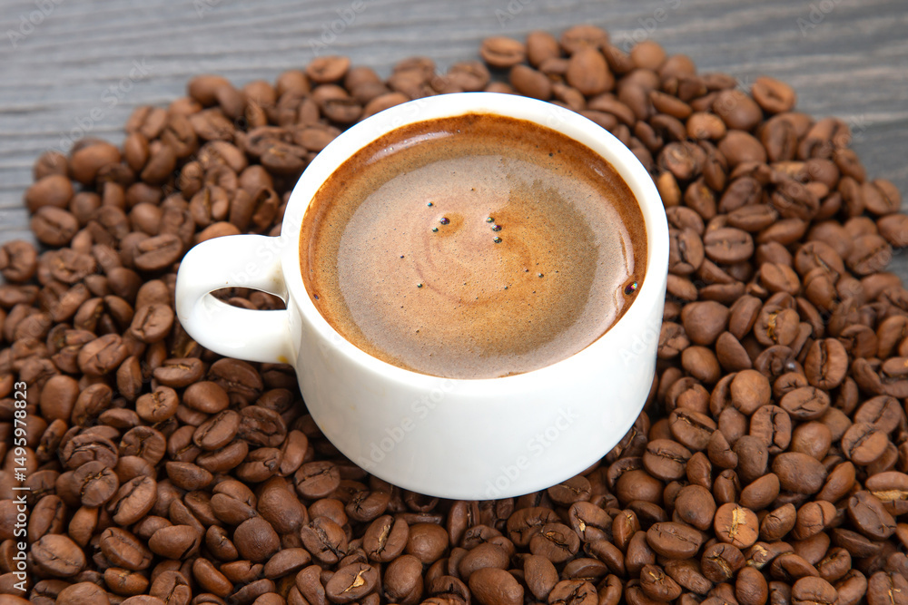 Fototapeta premium Dark espresso with a velvety crema fills a white cup on a saucer, surrounded by whole coffee beans, creating a cozy and aromatic coffee-themed composition