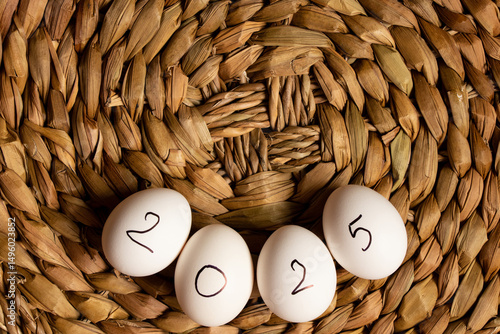 Eggs with the inscription 2025 lie on a straw wicker brown background