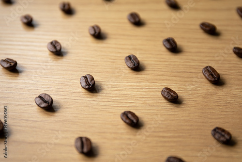 A collection of individual coffee beans is scattered over a wooden background, illuminated softly to emphasize texture and detail