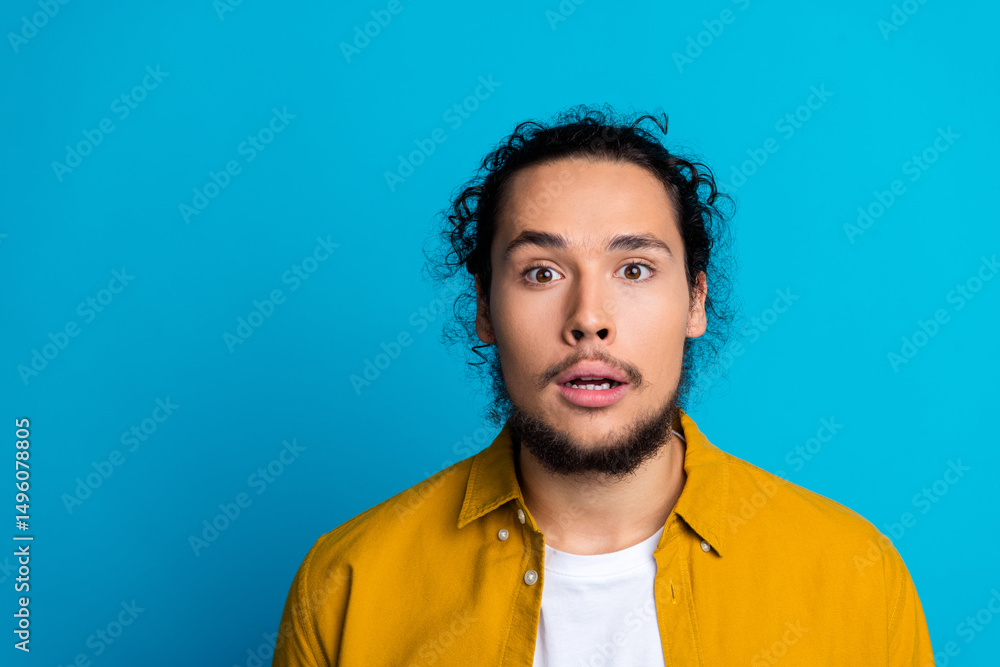 Fototapeta premium Surprised young man in a yellow shirt looking astonished against a vibrant blue background