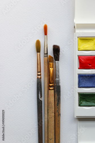 Paint brushes and box with watercolors on white paper background. Watercolor in box and brushes. Artist background. Painter materials. Aquarelle flat lay