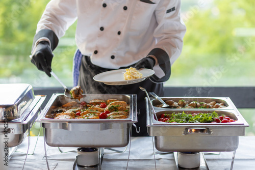 Chef serving a delicious buffet meal featuring grilled chicken, fresh vegetables, and flavorful sides at a catering event