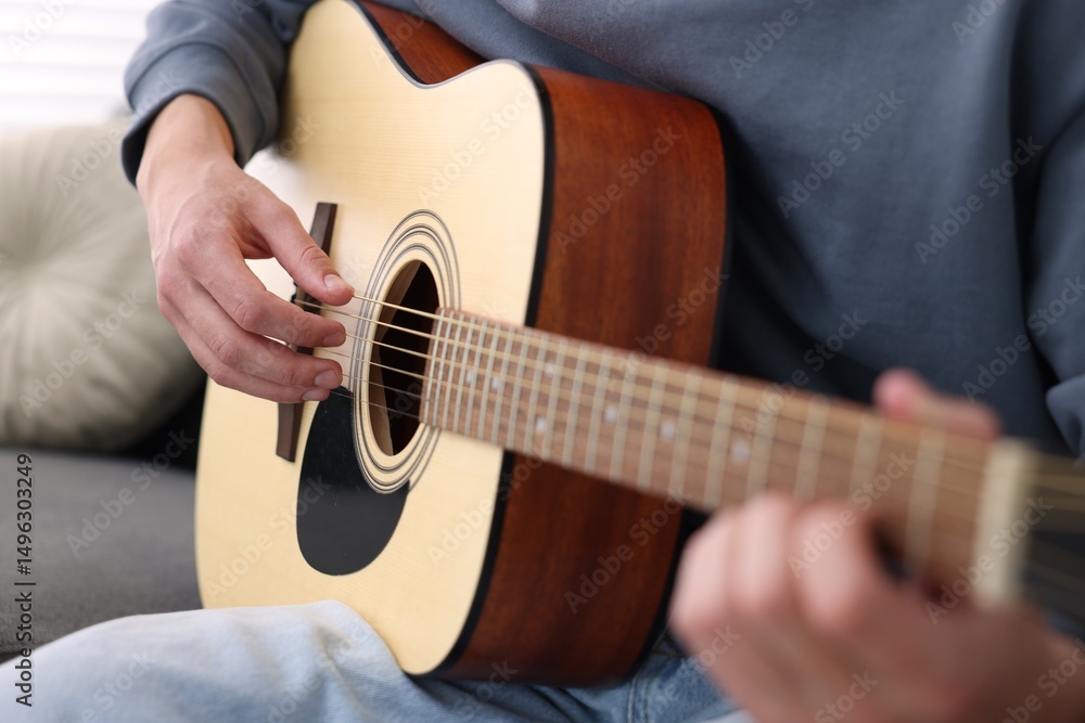 Fototapeta premium Young man playing guitar on sofa indoors, closeup