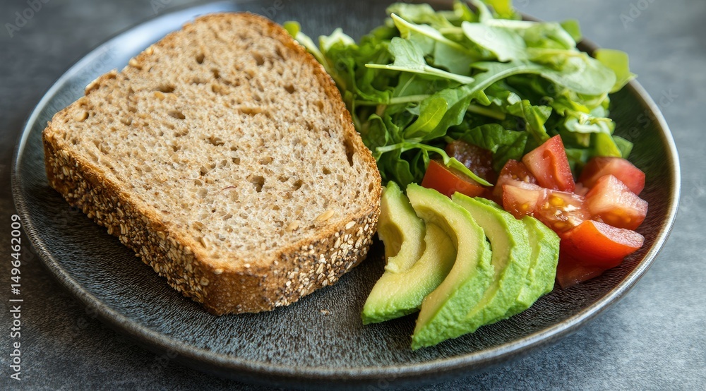 A dark-grey plate holds a slice of whole-wheat bread, alongside avocado slices and a vibrant salad of arugula and cherry tomatoes A dark-grey plate holds a slice of whole-wheat bread, alongside avocado slices and a vibrant salad of arugula and cherry tomatoes