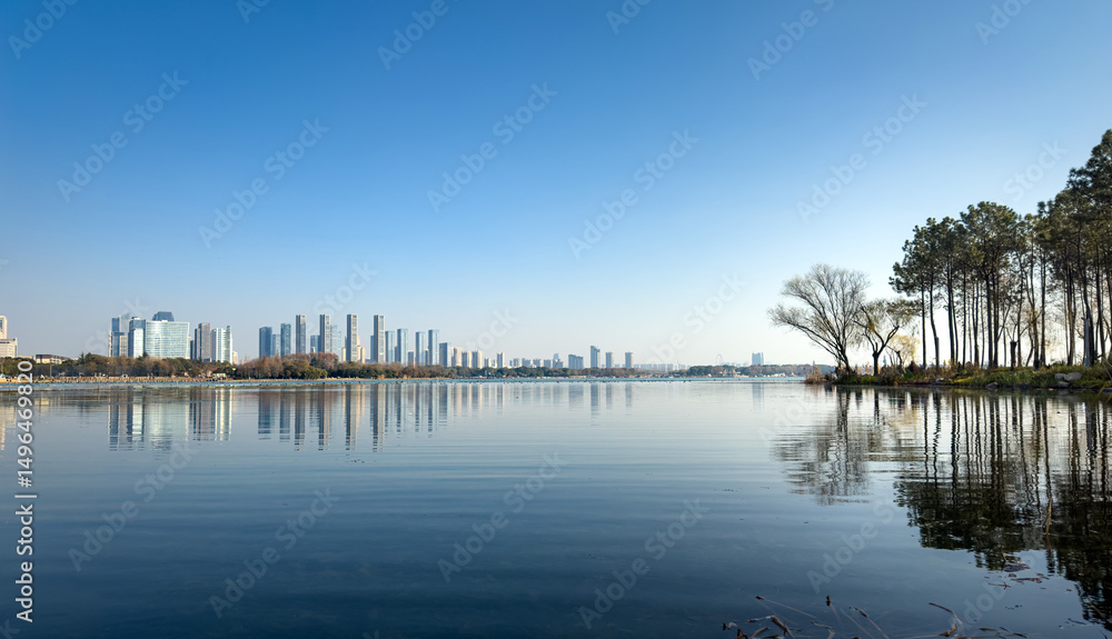 Obraz premium Tranquil Lakeside View with Modern City Skyline Under Clear Blue Sky