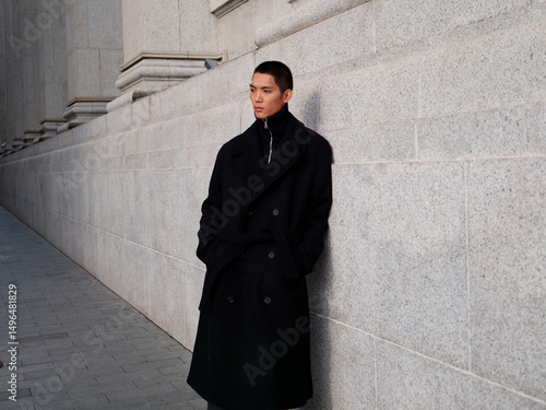 Portrait of handsome Chinese young man wearing black overcoat posing in the street, young guy with black short hair all in black with urban background. Male fashion, cool Asian young man lifestyle.