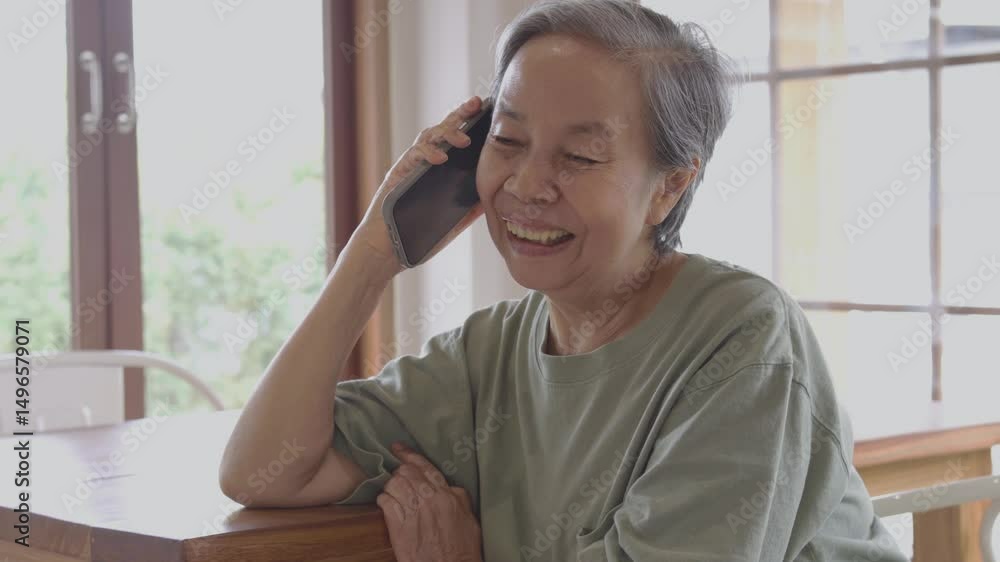 Mature Asian woman smiling while talking on the phone at home in natural light Mature Asian woman smiling while talking on the phone at home in natural light