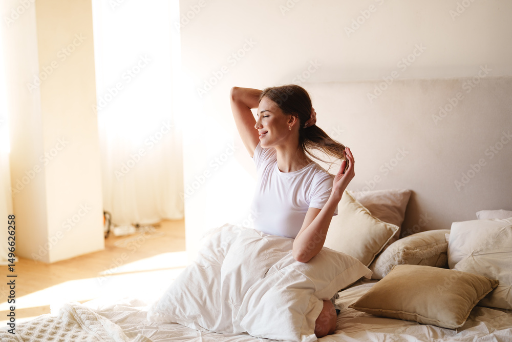 Woman stretching in morning light in cozy bedroom after waking up Woman stretching in morning light in cozy bedroom after waking up