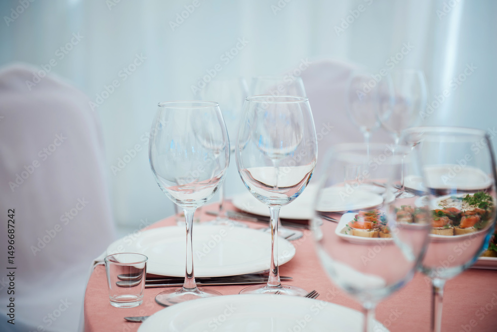 Fototapeta premium Preparation for the event at the restaurant. Wine glasses, glasses, plates, forks, knives on a light background and a pink tablecloth. Beautiful blurred background with copy space