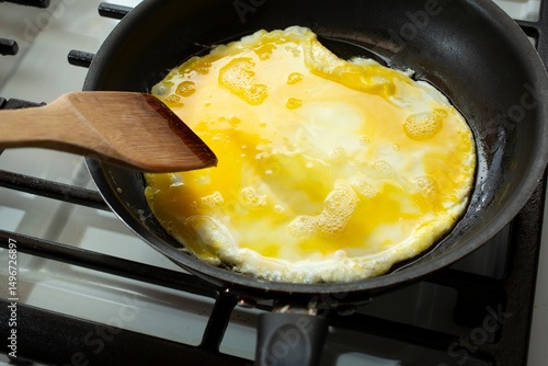 Cuadro en lienzo A view of a wooden spatula hovering over an omelet cooking in a non-stick pan