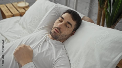 Young man sleeping peacefully in a cozy bedroom on a white bed with a serene expression and relaxed posture under soft indoor lighting.