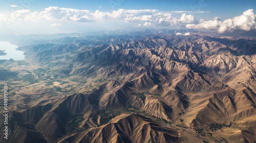 High above, a wide view of a canyon cutting through the land. Issyk Kul Lake is in sight. The scene shows rough, worn hills in Kyrgyzstan, Asia.
