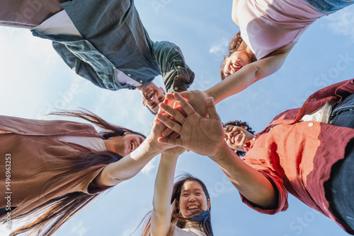 Multiethnic group of young friends stacking hands outdoors - Happy group of diverse young friends joining hands in a circle under the sky. Concept of teamwork, unity and youth friendship.