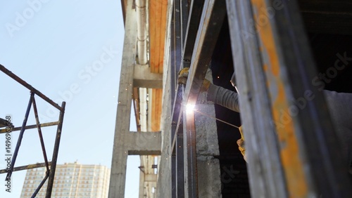 Construction worker welding metal frame on building site  with sparks flying