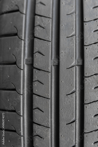 Vertical close-up view of a black rubber tire tread pattern, showing fine texture and directional grooves for grip and traction concepts.