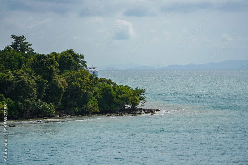 Naklejka premium Coastal Landscape Featuring Lush Green Island and Calm Waters Under a Cloudy Sky