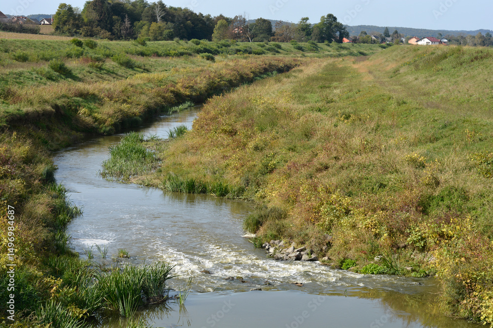 Obraz premium The Cesma River meanders westward through a grassy, rural landscape near Cazma
