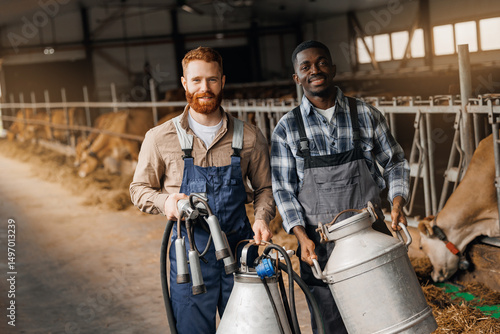 Two workers caucasian young man and African male with jug of milk and milking machine at cowhed. Farm business, industry of eco dairy factory