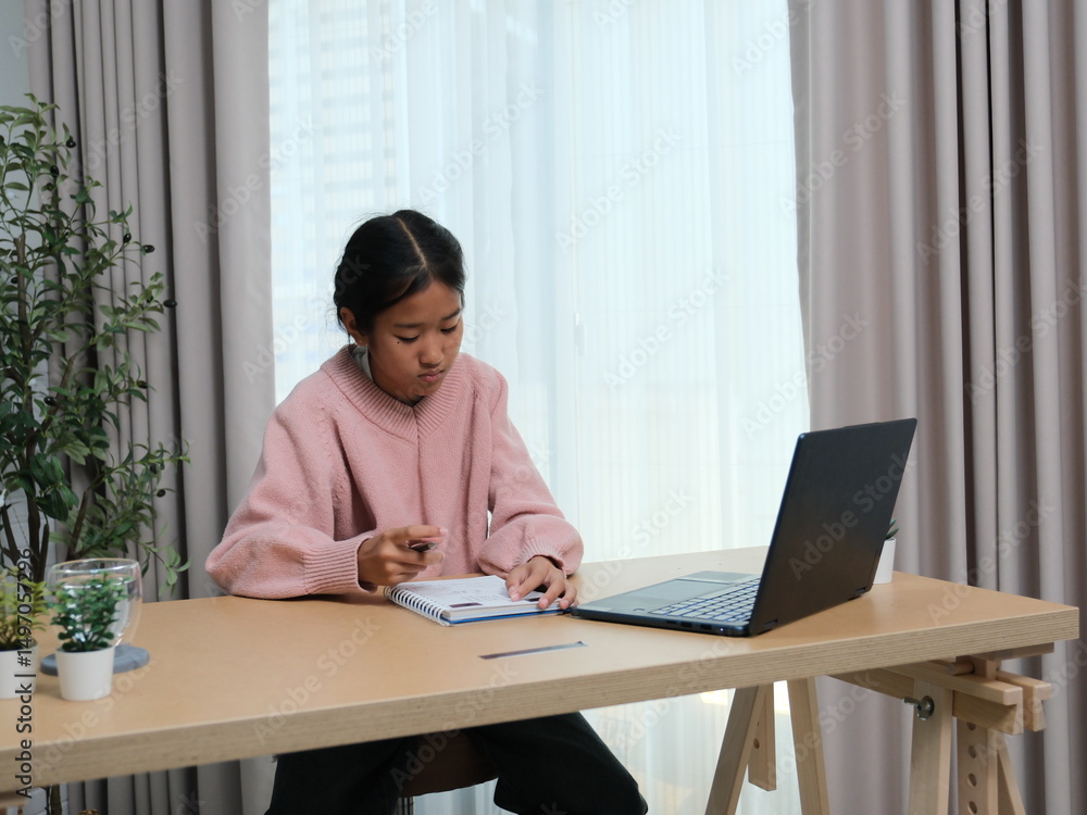 A girl is sitting at a desk with a laptop and a notebook A girl is sitting at a desk with a laptop and a notebook