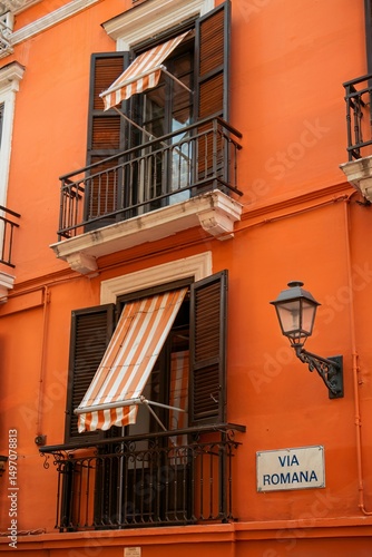 Bright Orange Building Exterior with Balconies and Striped Awnings, Italy