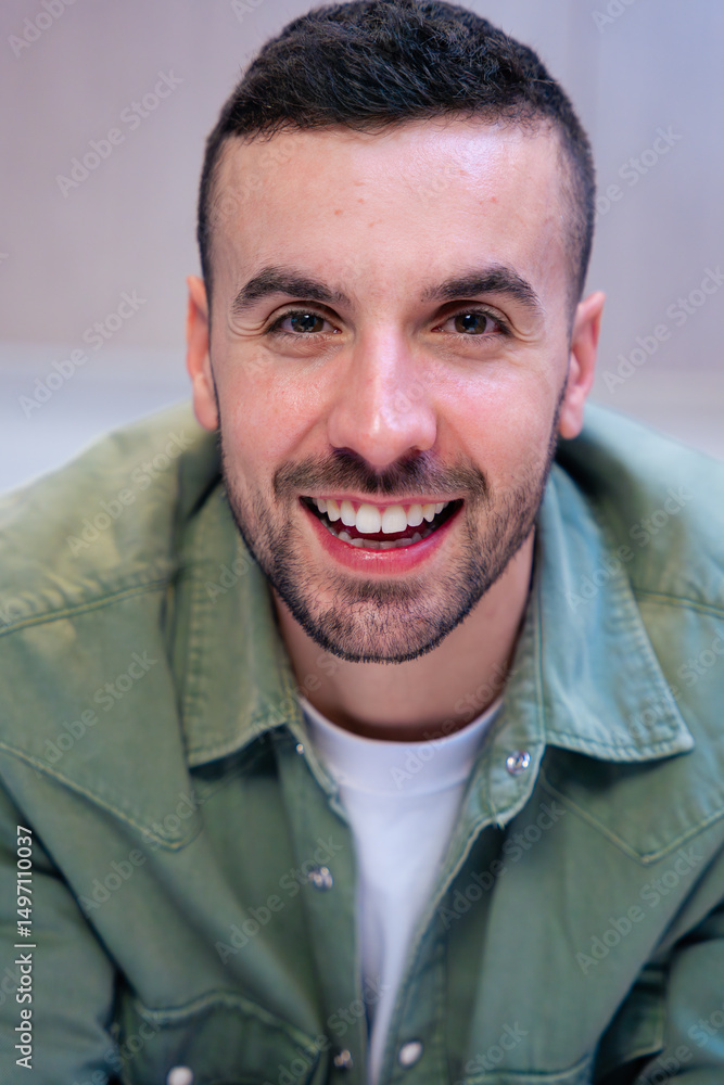 Fototapeta premium Vertical Portrait of a confident young caucasian man smiling at the camera in a stylish and bright kitchen interior, suggesting a relaxed and welcoming home atmosphere with visible food and cooking