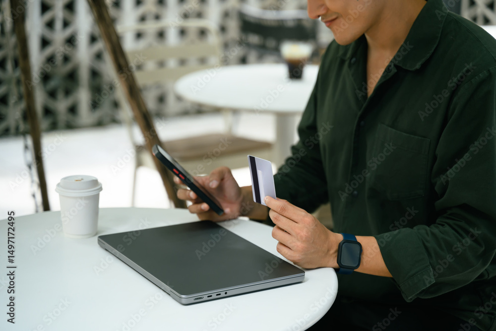 Obraz premium Man holding credit card and using smartphone for an online transaction at an outdoor cafe