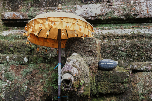 Golden umbrella and stone fountain at a sacred site in Bali, showcasing intricate details and lush greenery