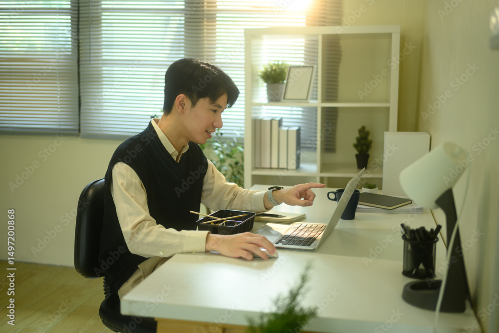 Smiling man eating instant noodles while working at his desk in a cozy, sunlit home office Smiling man eating instant noodles while working at his desk in a cozy, sunlit home office