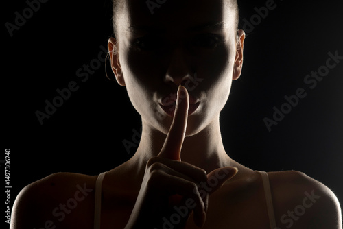 Fotografie Mysterious silhouette of a woman making 'shh' gesture with finger on lips